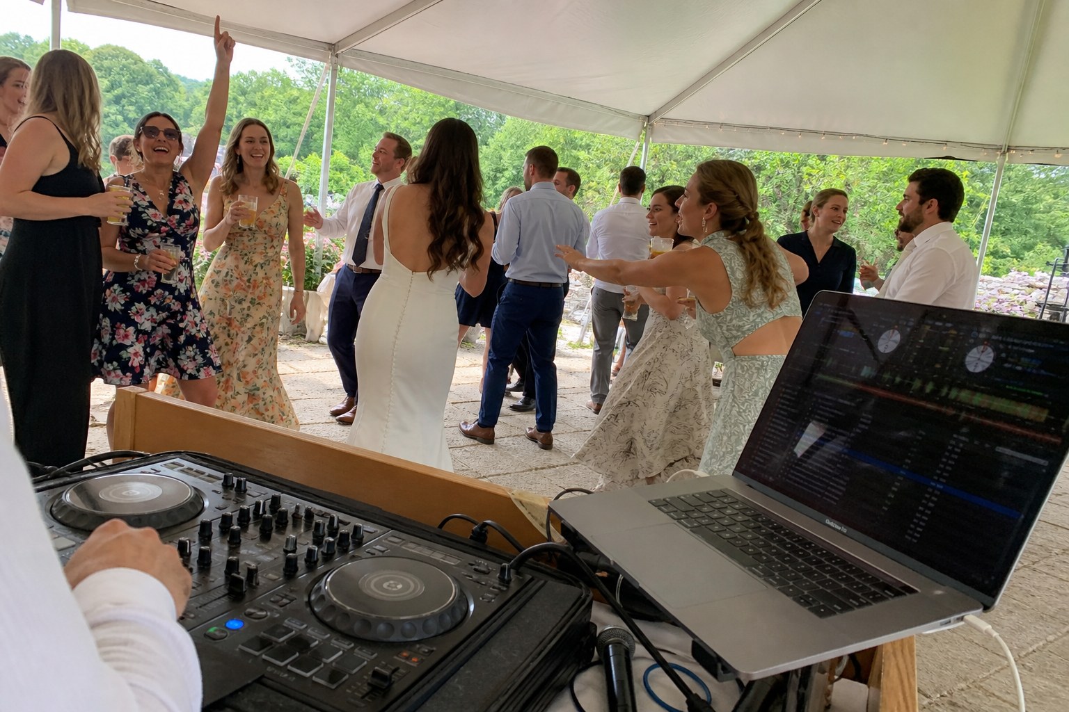 Candid view from a compact DJ setup toward guests dancing at a daytime tented wedding, shown as inspiration